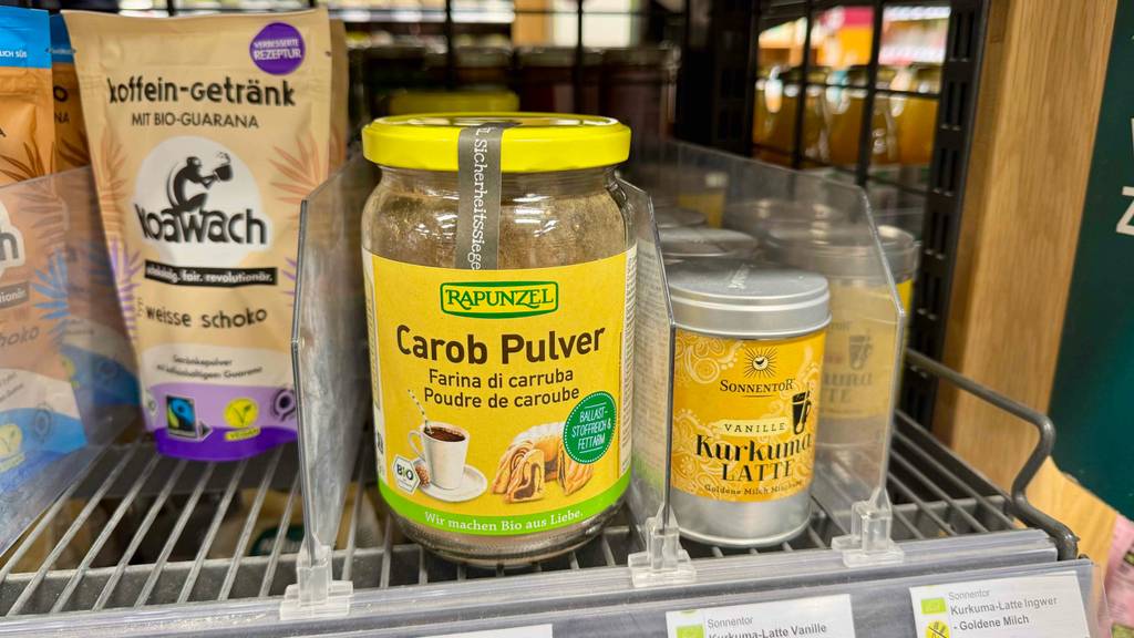 Carobpulver, getestet, im wiederverschließbaren Glas, steht neben weiteren Lebensmitteln auf einem Regal im Verkaufsbereich.