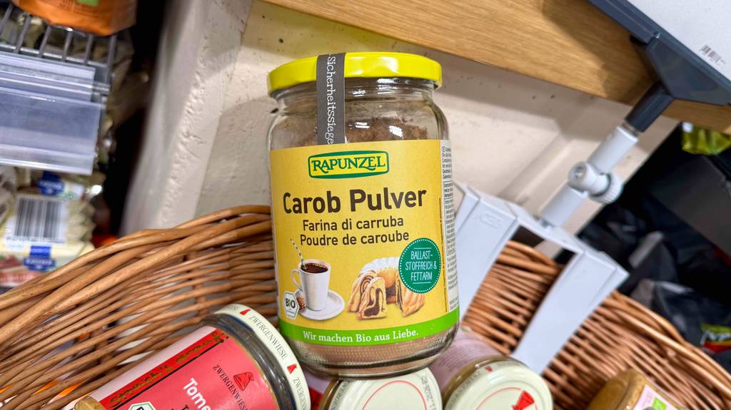 Im Test: Carobpulver im wiederverschließbaren Glas liegt in einem Korb auf anderen verpackten Lebensmitteln.