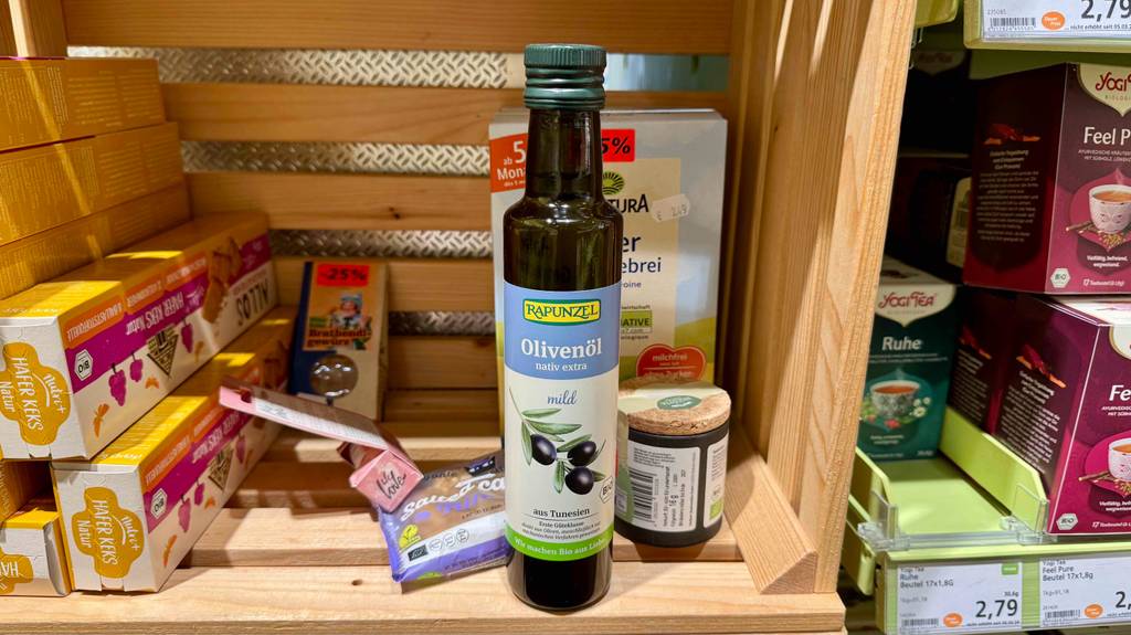 Mildes Olivenöl getestet: Eine Flasche steht zwischen verschiedenen Lebensmitteln in einer Holzkiste.