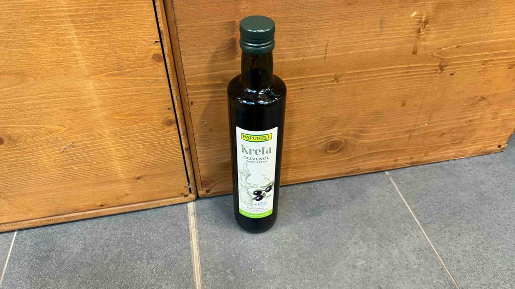 Eine Flasche Olivenöl Kreta steht zum Testen vor einer Holzwand.