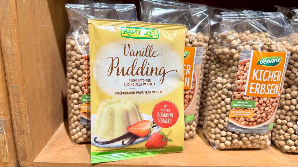 Vanillepuddingpulver im Test: Eine Tüte mit Pulver und echter Bourbon-Vanille steht auf einem Regal vor Kichererbsen-Packungen.