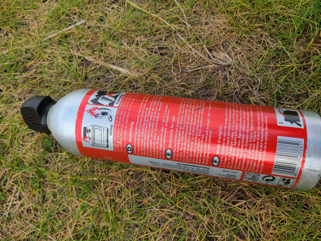 Ein getesteter Auto-Feuerlöscher liegt mit der Rückseite mit Anleitung nach oben auf einer Rasenfläche.
