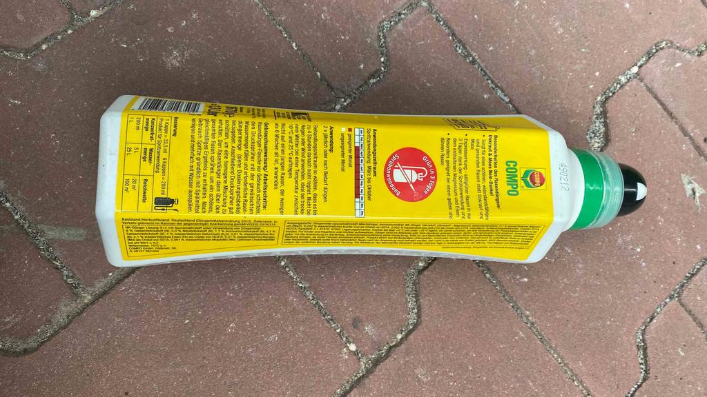 Eine Flasche getesteter Rasendünger liegt auf einem Steinboden. 