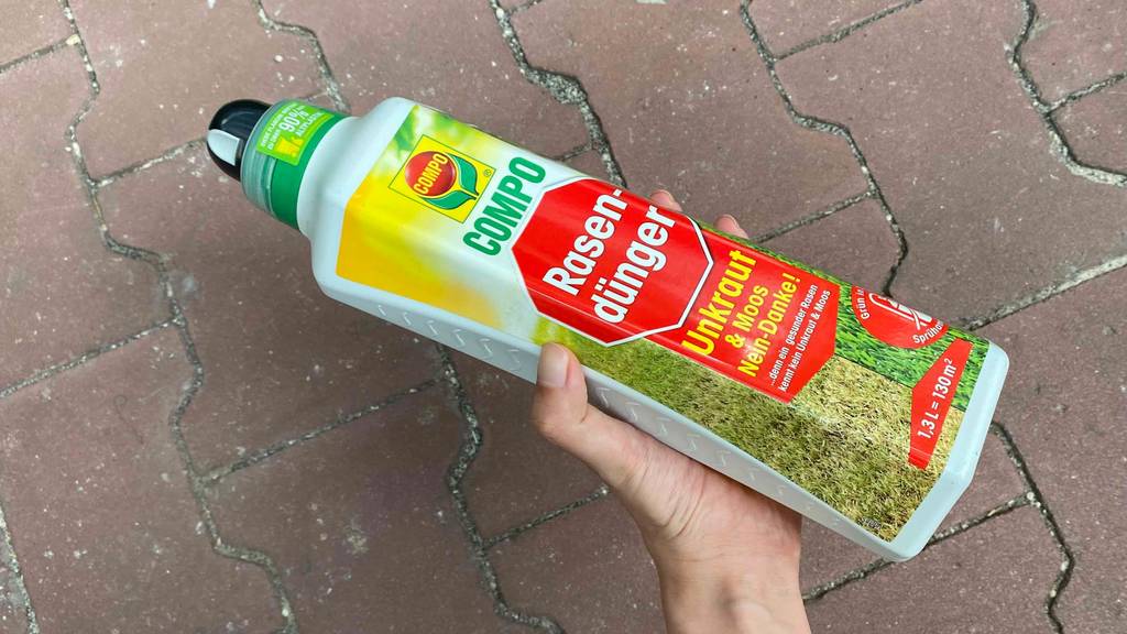 Ein getesteter Rasendünger in einer Flasche wird gehalten vor einem Steinboden.