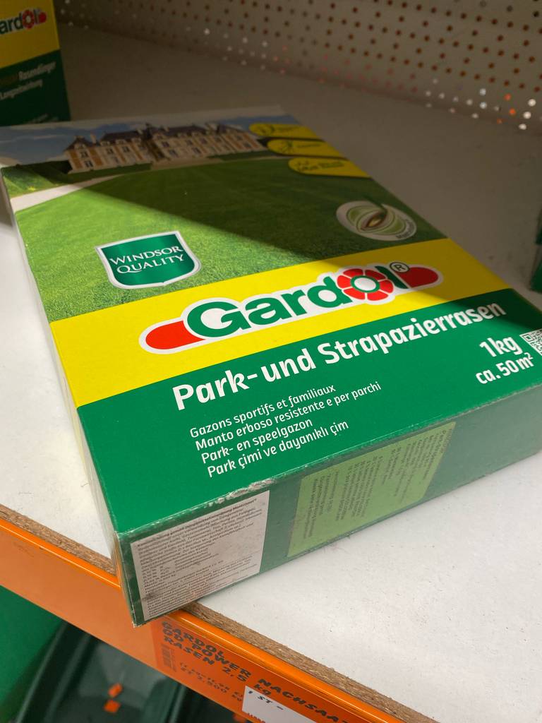 Eine Packung mit getestetem Rasensamen für Park- und Strapazierrasen liegt in einem Regal. 