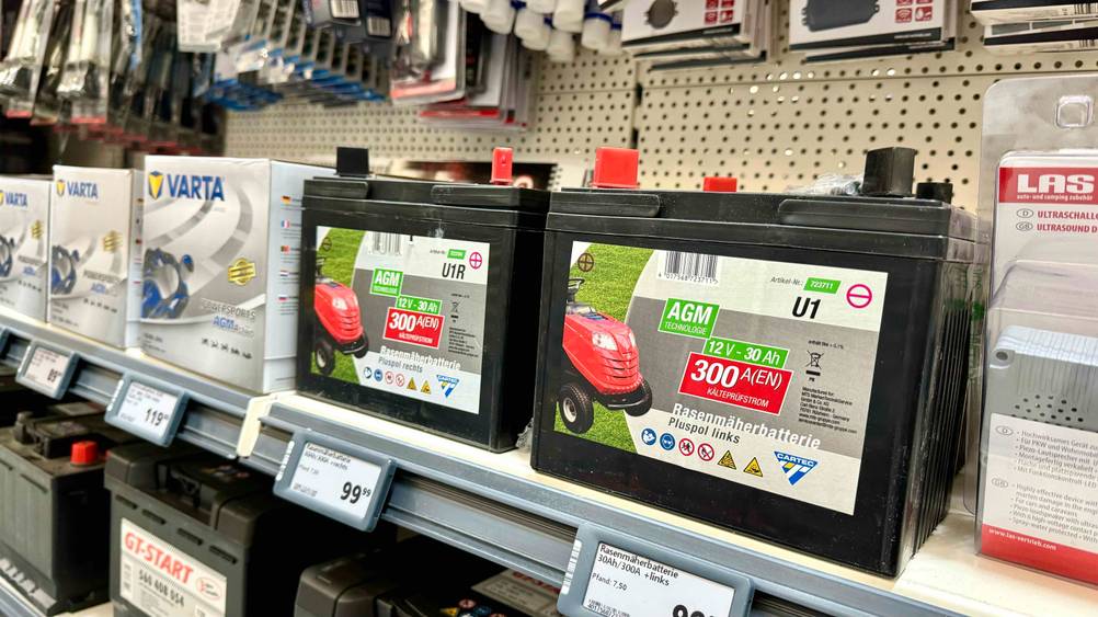 Zwei getestete Rasentraktor-Batterien nebeneinander mit Preisschild in einem Verkaufsregal neben anderen Produkten.