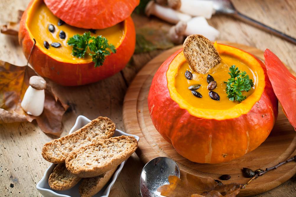 In 2 ausgehölten Kürbissen ist Kürbissuppe mit geröstetem Brot serviert.