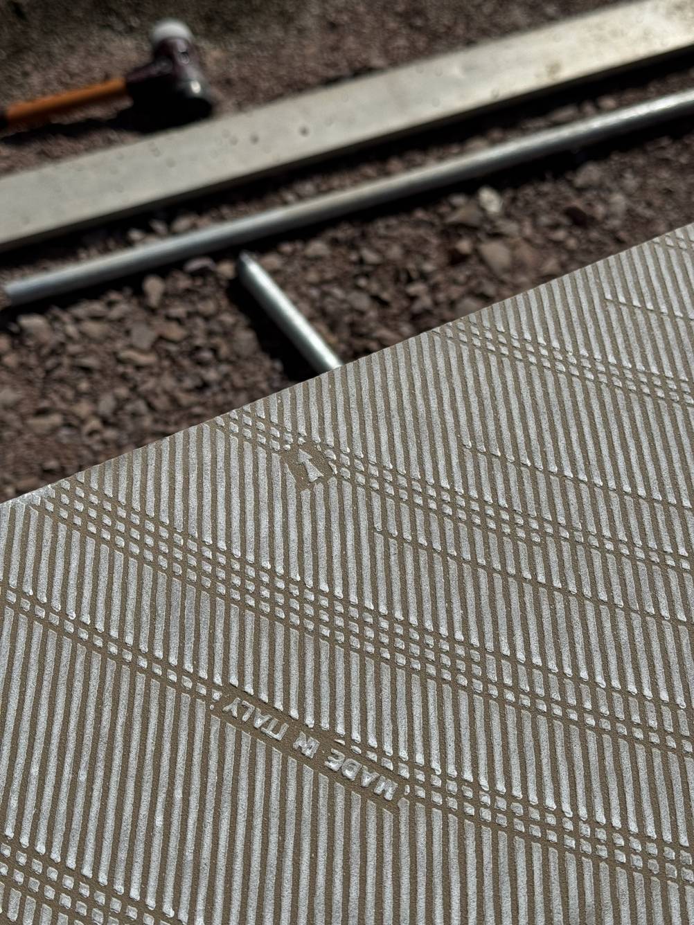 Auf der Unterseite einer Terrassenplatte ist ein kleiner Pfeil abgedruckt, der zu einer Außenkante der Platte zeigt.