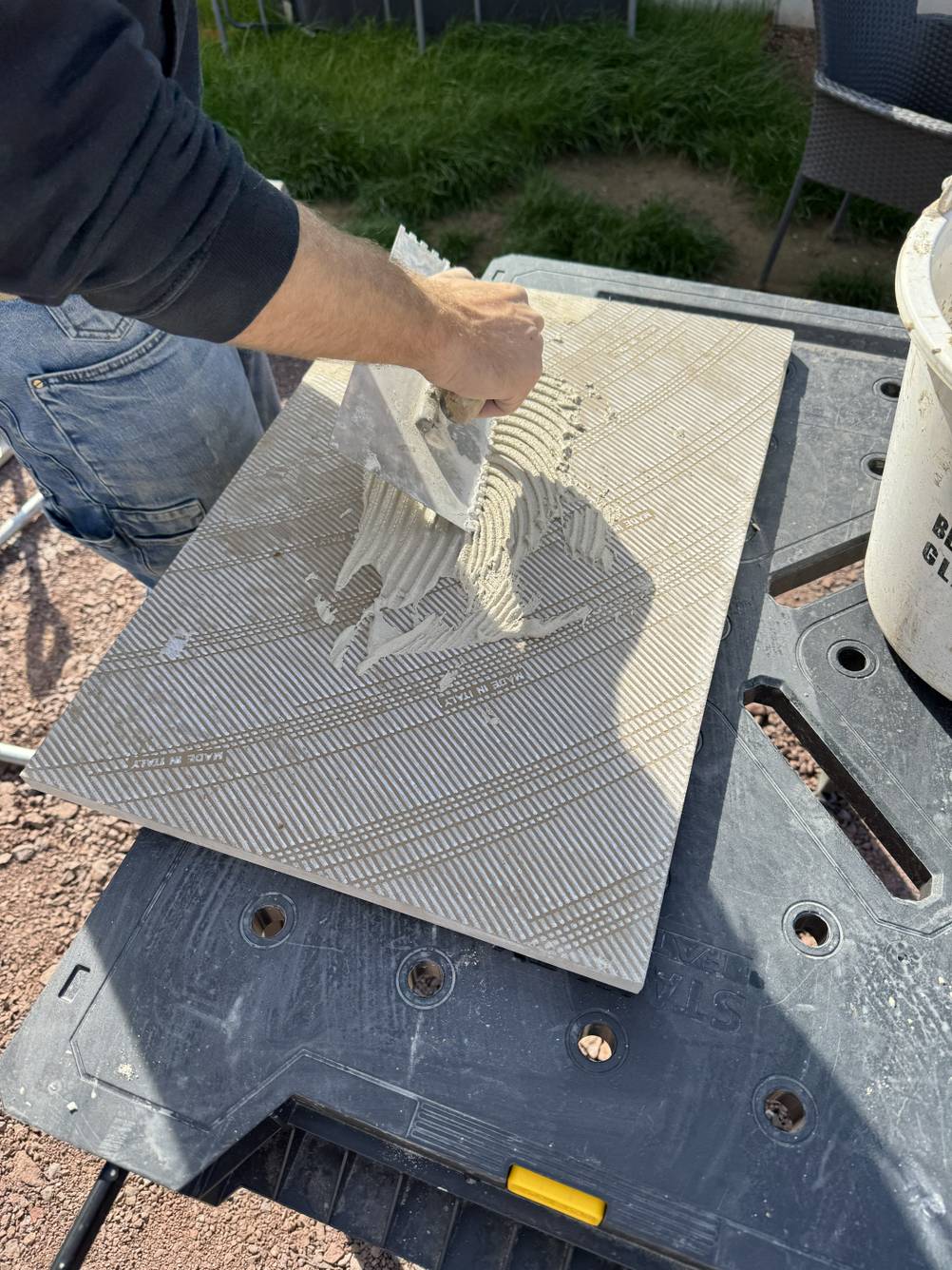 Auf den Untergrund einer Terrassenplatte wird Kleber aufgetragen.