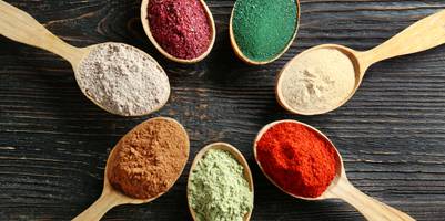 7 verschiedene Superfood-Pulver liegen in Holzlöffeln in einem Kreis.