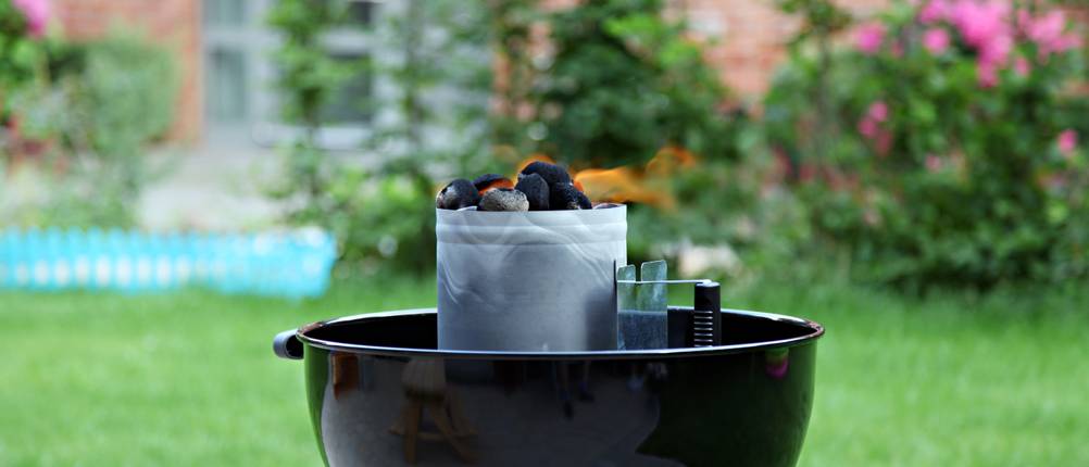 Grill, auf dem brennende Kohle in einem Anzündkamin erhitzt wird, steht in einem Garten.