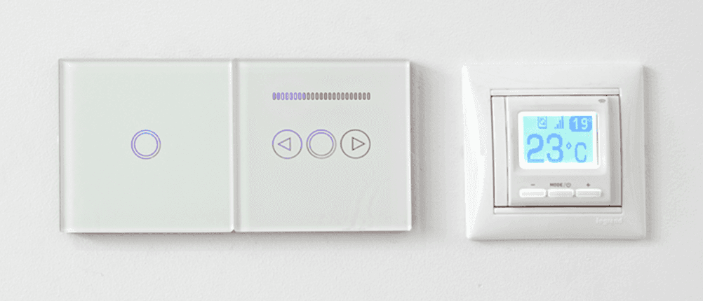 Raumthermostat für die Fußbodenheizung im Test: Ein Raumthermostat für die Fußbodenheizung hängt neben weiteren Touch-Displays an einer Wand.