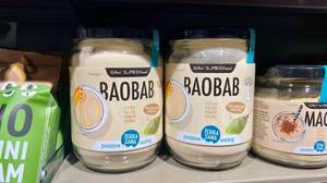Baobab im Test: Transparente Gläser mit Baobab-Pulver und schwarzem Schraubverschlüssen stehen in einem Verkaufsregal inmitten anderer Lebensmittel.