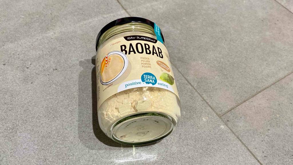 Baobab-Test: Ein transparentes Glas mit Baobab-Pulver und schwarzem Schraubverschluss liegt auf einem grauen Fliesenboden.