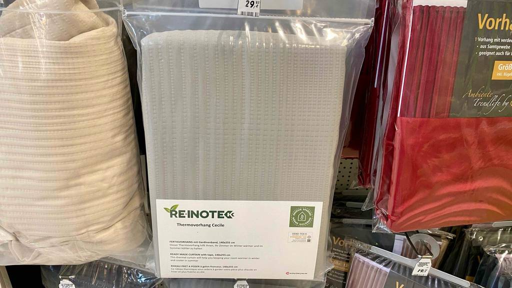 Thermovorhang im Test: ein hellgraues Stoff-Modell von Re-inote hängt in durchsichtigem Kunststoff eingeschweißt an einem Verkaufsstand mit anderen Vorhängen.