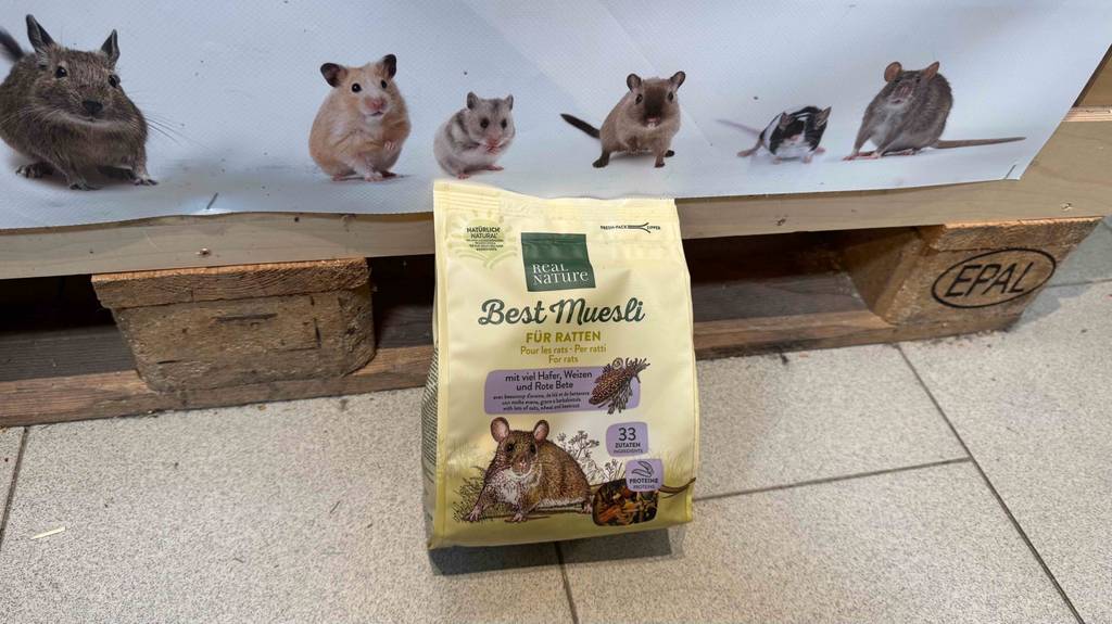 Eine Packung Rattenfutter steht zum testen vor einem Plakat mit Nagetieren.