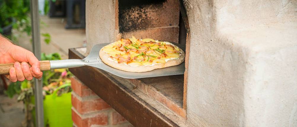 Eine Person schiebt eine belegte Pizza in einen Outdoor-Pizzaofen.