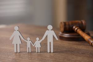 Rechtsschutzversicherung-Test: Figuren einer Familie bestehend aus Mutter, Vater und zwei Kindern, stehen auf einem Tisch neben einem Richterhammer.