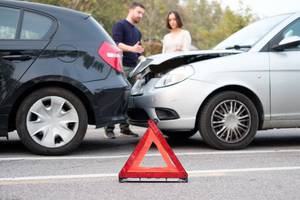 Test der Rechtsschutzversicherungen: Ein Mann und eine Frau stehen nach einem Unfall neben ihren Fahrzeugen und diskutieren, im Vordergrund steht ein Warndreieck.