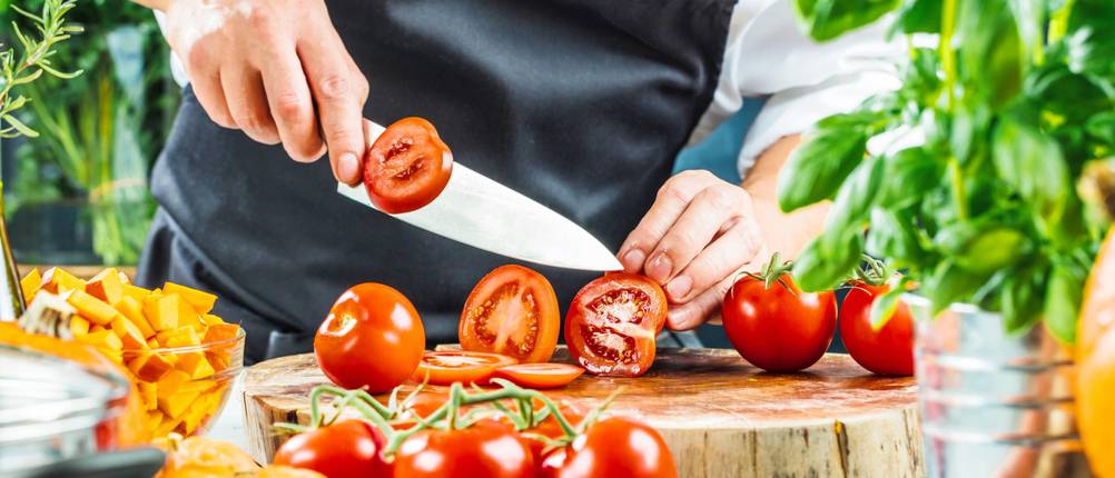 Red-Spirit-Messer im Test: Frau schneidet Tomaten in Scheiben auf einem Holzbrett.