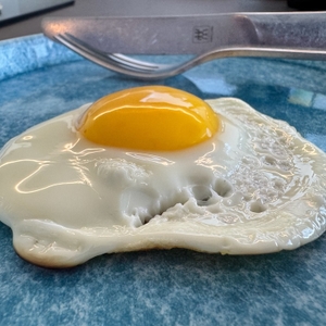 Fertiges Spiegelei in Nahaufnahme mit einer Gabel im Hintergrund