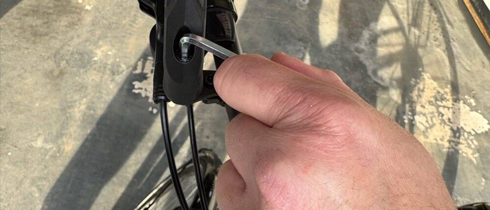Eine Hand befestigt den Reezer RS1 mit einem Innensechskantschlüssel an einem Fahrradlenker.