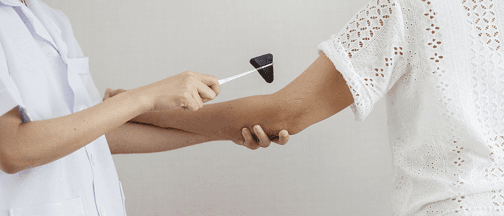 Reflexhammer im Test: Ärztin schlägt mit einem Reflexhammer auf dem Ellenbogen einer Patientin