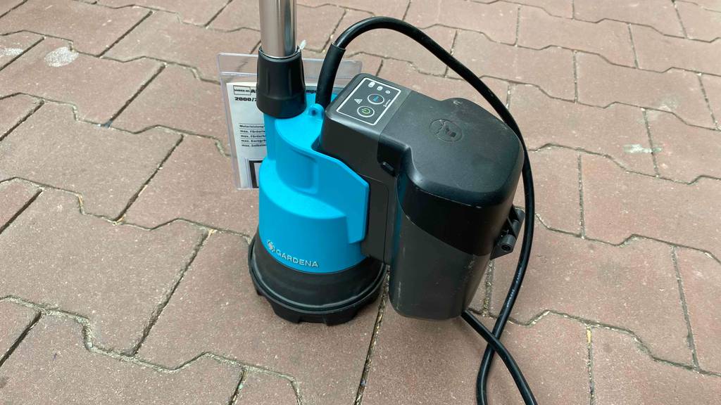 Eine getestete Regenfasspumpe mit Kabel befindet sich auf dem Boden. 