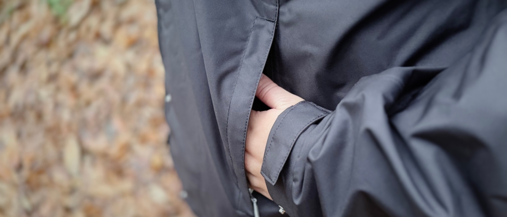 Eine Hand in der linken Jackentasche der schwarzen Helly Hansen Damen-Regenjacke.