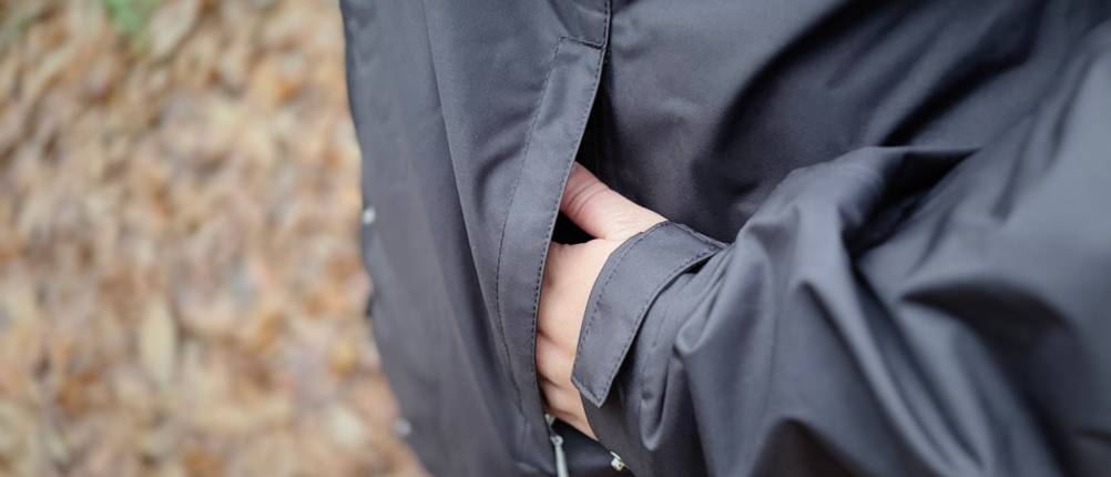 Eine Hand in der linken Jackentasche der schwarzen Helly Hansen Damen-Regenjacke.