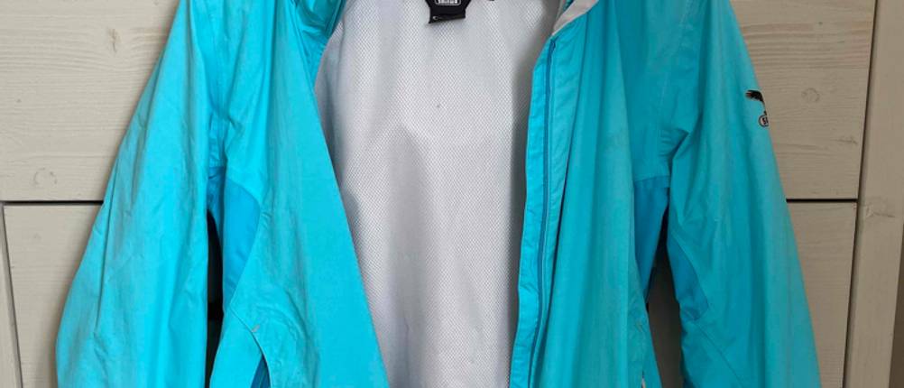 Regenjacke Salewa für Damen in Türkis hängt auf einem Kleiderbügel an einem Schrank.