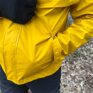 Eine Person steckt die Hand in die Seitentasche der Helly Hansen Moss Regenjacke. Die Tasche ist mit einer Klappe geschützt.