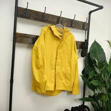 Eine gelbe Helly Hansen Moss Regenjacke hängt an einer Holzgarderobe