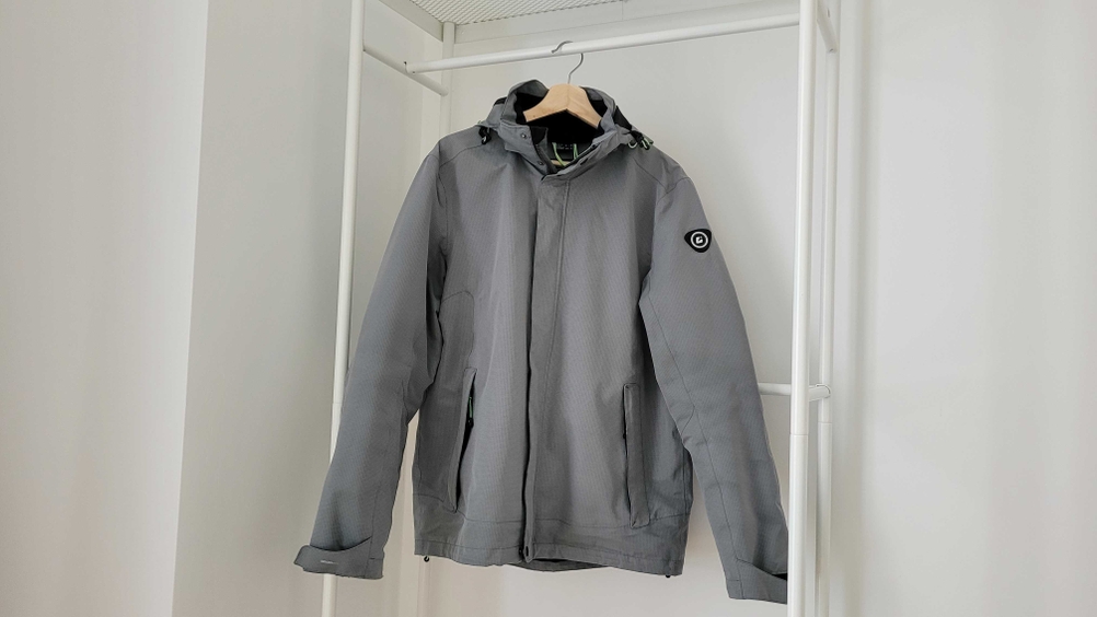 Eine getestete Regenjacke für Herren hängt auf einem Bügel in einem weißen Gestell.