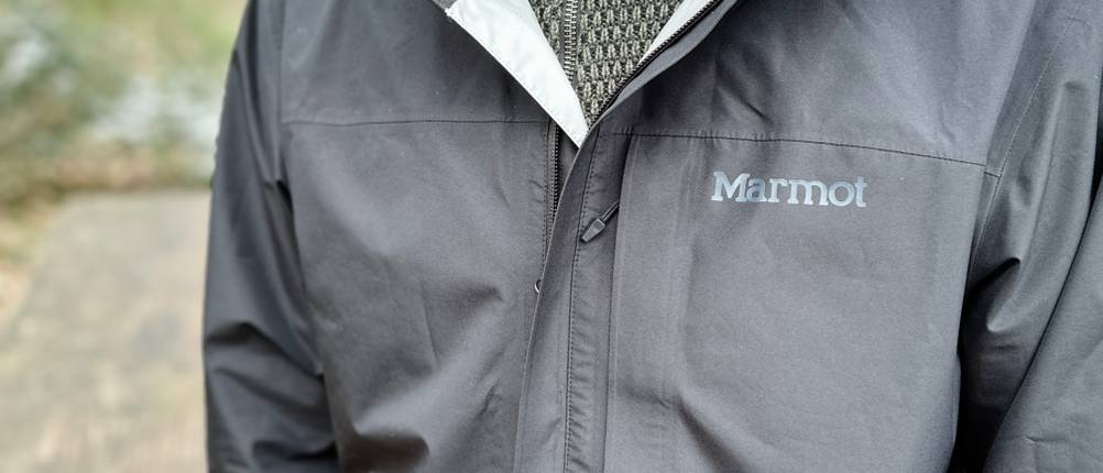 Die Marmot Minimalist Regenjacke in Schwarz wird über einem Strickpullover getragen. Das Markenlogo ist auf der Brust sichtbar, während die Jacke leicht geöffnet ist.