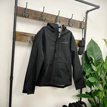 Die schwarze Marmot Minimalist Regenjacke hängt auf einem Bügel an einer Garderobe