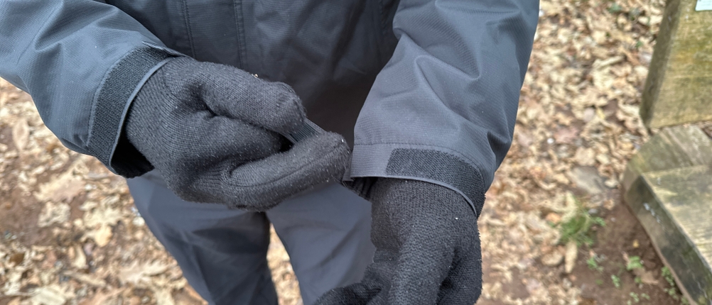 Ein Mann stellt den Klettverschluss am Ärmel der Vaude Escape Light Regenjacke ein. Die Handschuhe bleiben dabei angezogen.