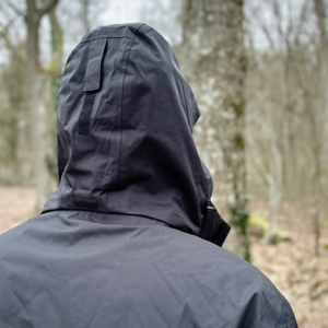 Die Kapuze der Vaude Escape Light Regenjacke von hinten in einer Outdoor-Umgebung. Sie ist großzügig geschnitten und mit einem Klettriemen verstellbar.