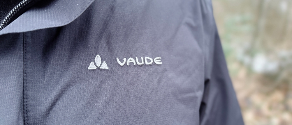Nahaufnahme des Vaude Logos auf der Brust der Escape Light Regenjacke. Die Jacke wird über einem warmen Pullover getragen.