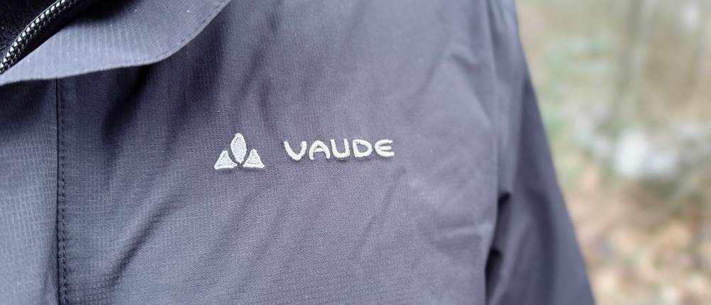 Nahaufnahme des Vaude Logos auf der Brust der Escape Light Regenjacke. Die Jacke wird über einem warmen Pullover getragen.