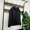 Eine schwarze Vaude Escape Light Regenjacke hängt an einer rustikalen Garderobe