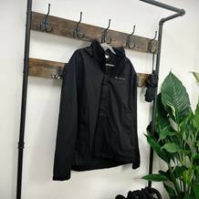 Eine schwarze Vaude Escape Light Regenjacke hängt an einer rustikalen Garderobe