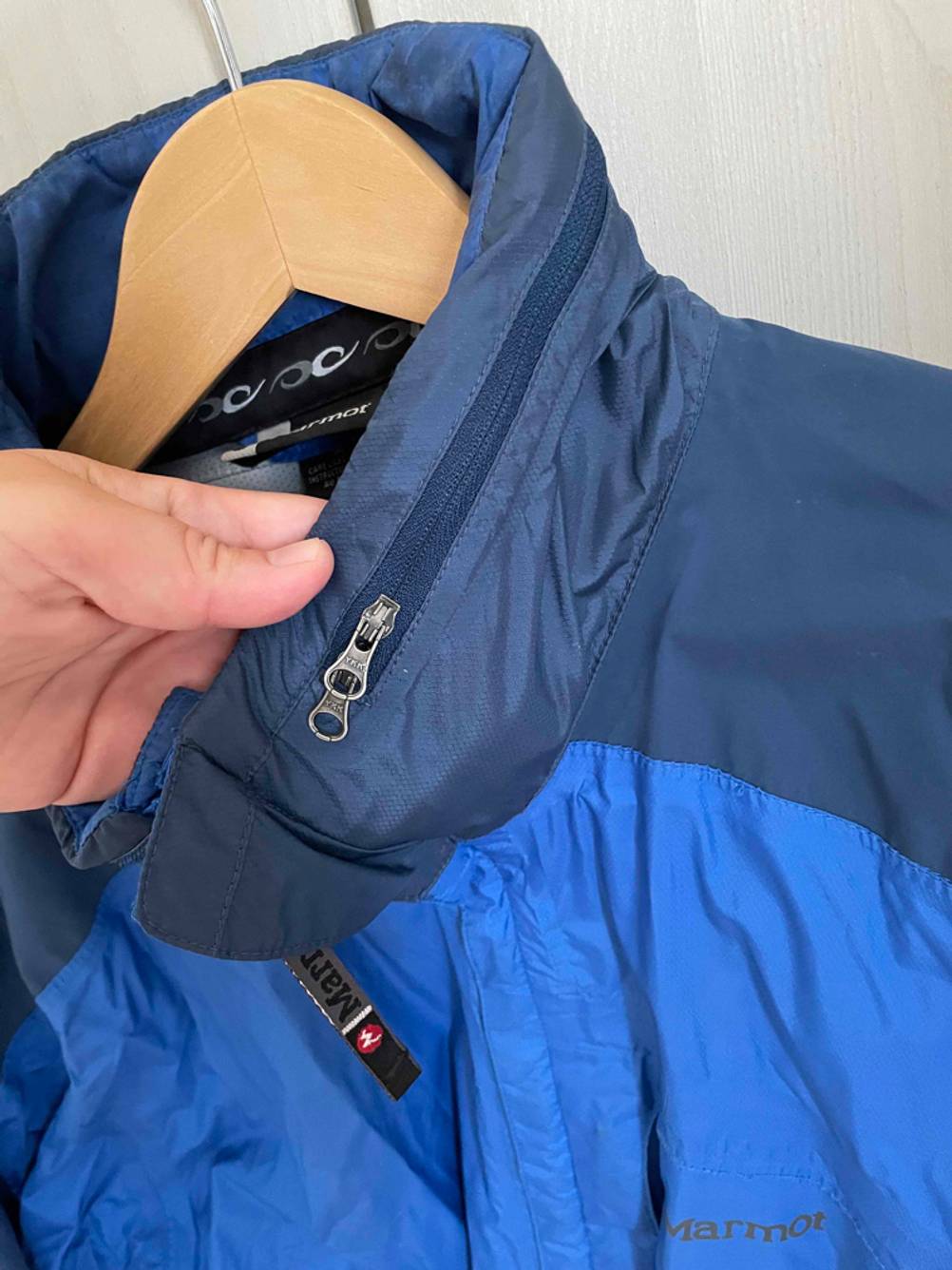 Unisex-Regenjacke-Test: Eine blaue Unisex-Regenjacke mit Kapuzenfach hängt auf einem Kleiderbügel. 