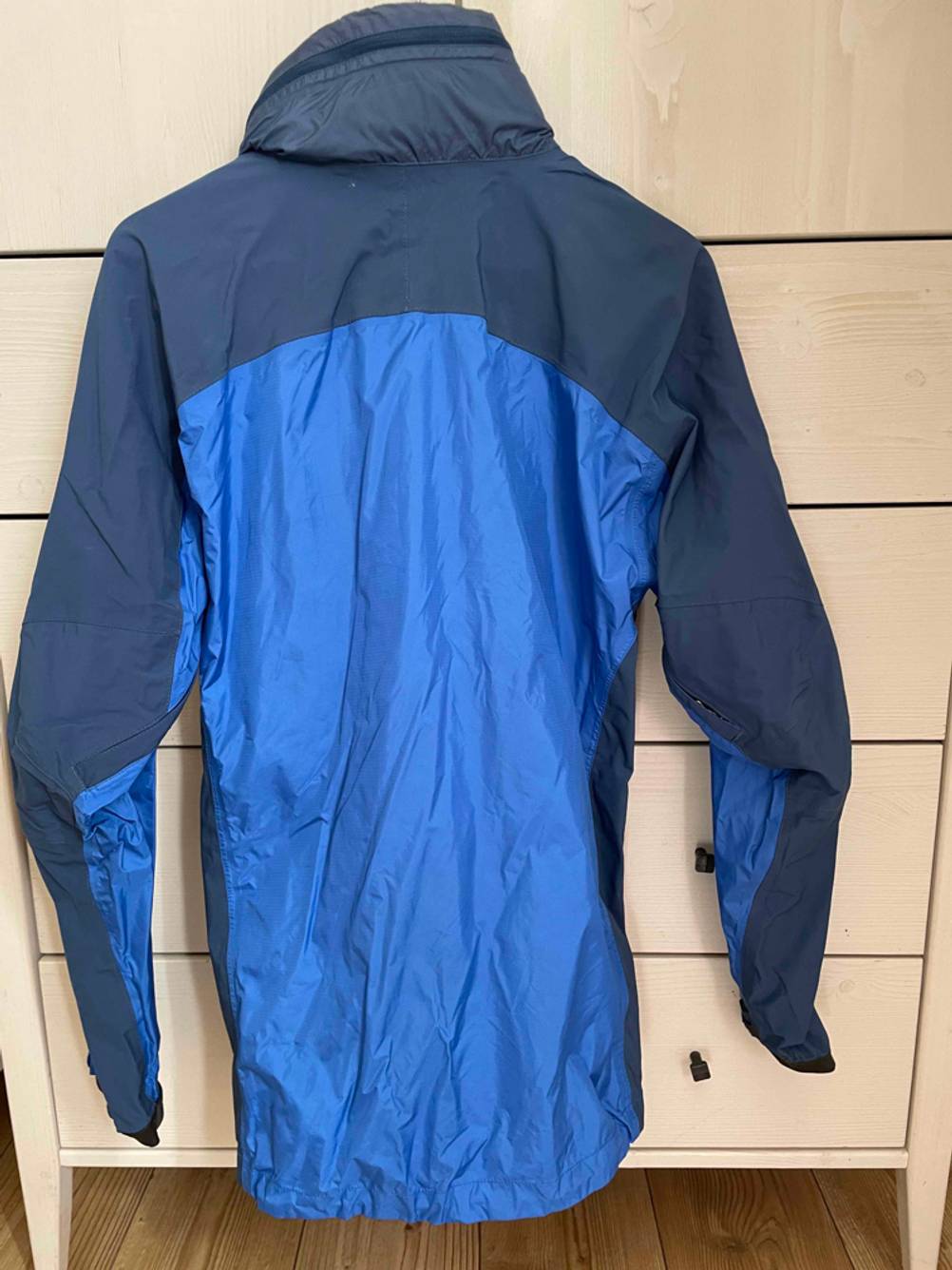 Regenjacke-Unisex-Test: Eine blaue Unisex-Regenjacke hängt an einem Schrank. 