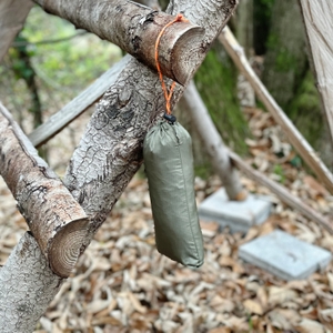 Der Anyoo-Regenponcho hängt in seinem grauen Beutel an einem Rahmen im Wald.