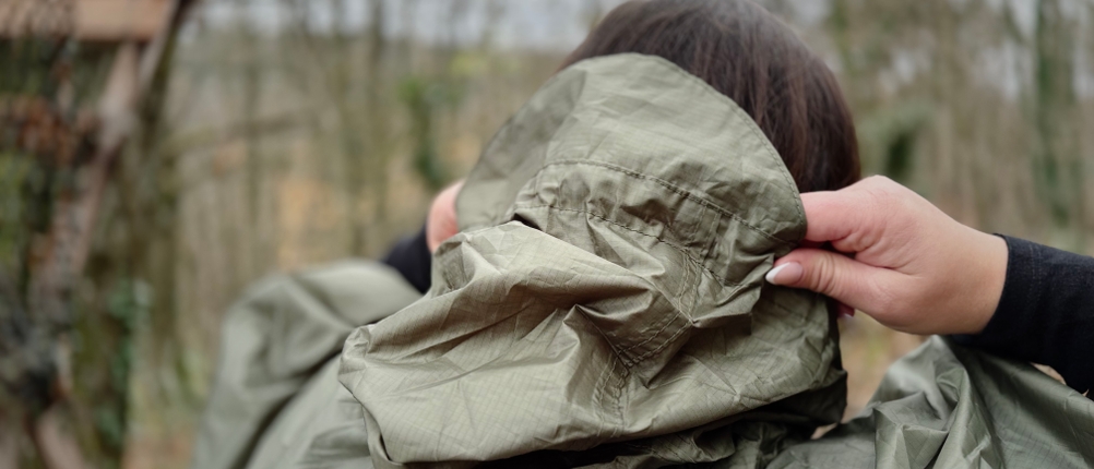 Die Person zieht die Regenkapuze gerade über den Kopf und zeigt den Schirm am vorderen Rand der Kapuze.