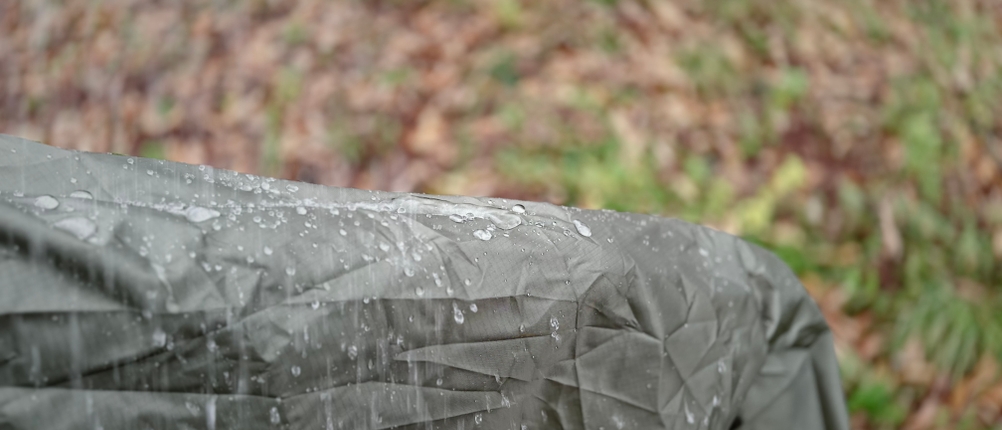 Eine Person trägt den grauen Anyoo-Regenponcho und zeigt, dass die Regentropfen bei gehobenem Arm augenblicklich abperlen.