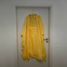 Der gelbe AWHA-Regenponcho hängt auf einer Bügel am Türrahmen.