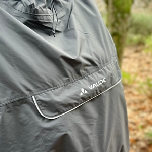 Der große Brustbeutel des Vaude-Regenponchos mit reflektierenden Zierstreifen ist auf Brusthöhe zu sehen.
