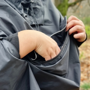 Die Person verstaut Gegenstände in der Brusttasche des Vaude-Regenponchos.
